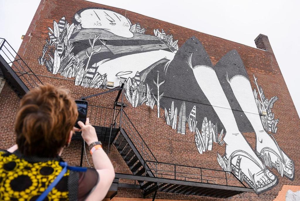 Woman taking a picture of a mural on a brick wall
