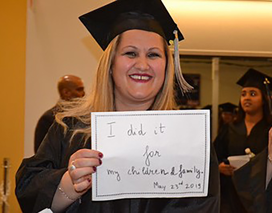 Woman graduating and holding a sign that says "I did it for my children and family"
